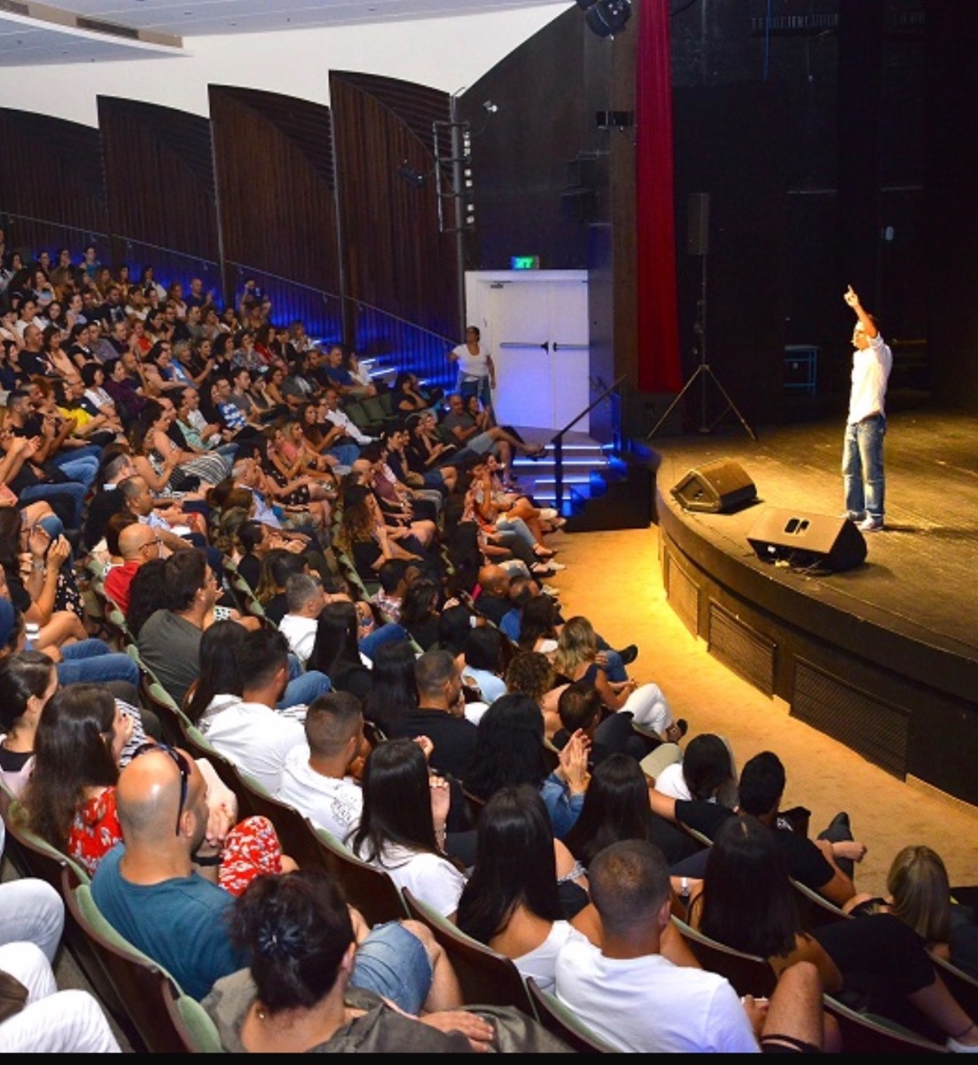 סטנדאפיסט על במה מופיע מול מסך המציג נתוני בינה מלאכותית