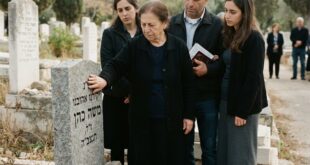 ידיים נוגעות במצבה עם כיתוב חרוט באבן בבית עלמין